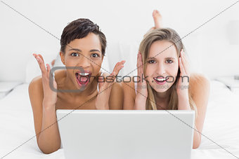 Shocked young female friends with laptop in bed