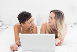 Cheerful female friends with laptop in bed