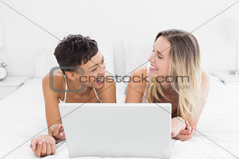 Cheerful female friends with laptop in bed