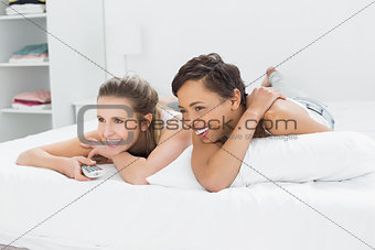 Cheerful female friends with remote control lying in bed