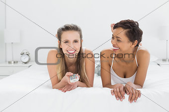 Relaxed female friends with remote control lying in bed