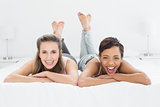 Cheerful young female friends lying in bed