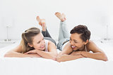 Two smiling female friends lying in bed