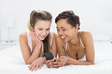 Smiling female friends reading text message in bed