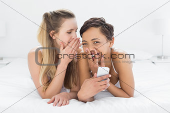 Cheerful relaxed female friends gossiping in bed