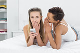 Two relaxed female friends gossiping in bed