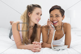 Cheerful female friends using phone while lying in bed