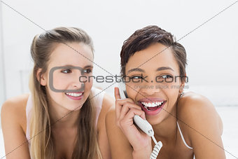 Close-up of cheerful female friends using phone in bed