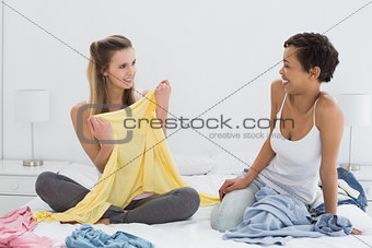 Pretty female friends selecting clothes in bed