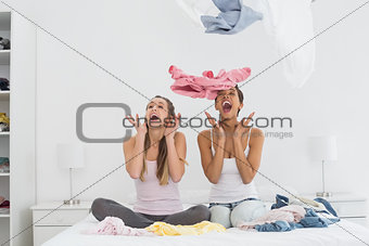 Surprised female friends with clothes up on bed