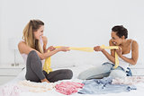 Female friends jokingly fighting over clothes on bed