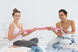 Pretty friends jokingly fighting over clothes on bed