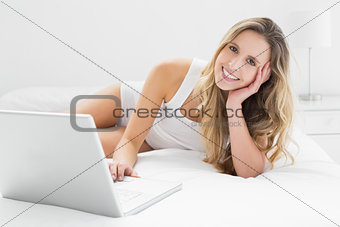 Smiling young woman using laptop in bed