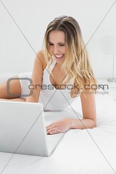 Smiling pretty woman using laptop in bed