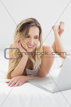 Pretty young woman looking at laptop in bed