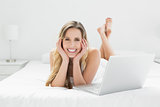 Smiling young woman with laptop lying in bed