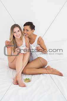 Young female friends with coffee cups in bed