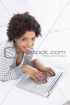 Smiling young woman using laptop in bed