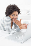 Shocked woman with coffee cup using laptop in bed
