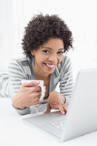 Smiling woman with coffee cup using laptop in bed
