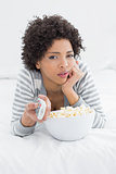 Woman with remote control and popcorn bowl lying in bed