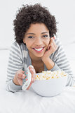 Smiling woman with remote control and popcorn bowl in bed