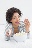 Cheerful woman with remote control and popcorn bowl in bed