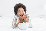 Cheerful woman with remote control and popcorn bowl in bed