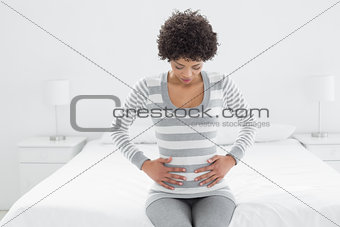 Casual woman with stomach pain sitting in bed