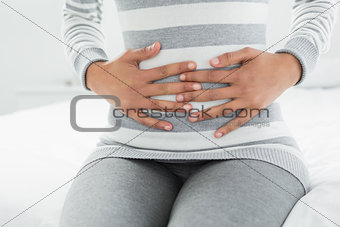 Mid section of a woman with stomach pain sitting in bed