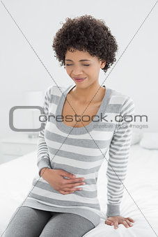 Casual woman with stomach pain sitting in bed