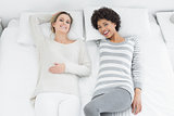 Portrait of casual female friends lying in bed