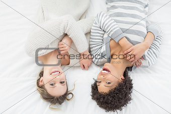 Two casual young female friends lying in bed