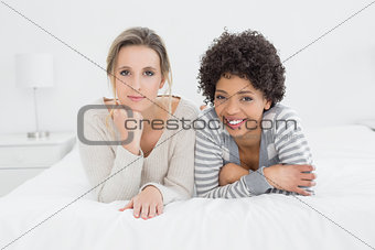 Two smiling young female friends lying in bed