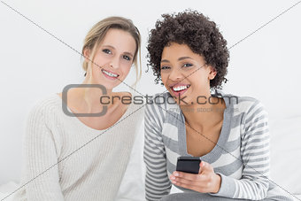 Smiling female friends reading text message on bed