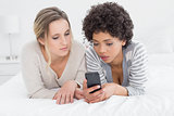 Serious female friends reading text message in bed