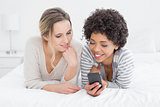 Smiling female friends reading text message in bed