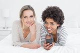 Two smiling female friends reading text message in bed