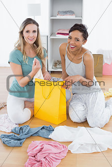 Two smiling women sitting on floor with shopping bag