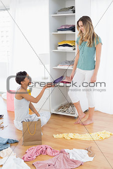 Happy young women arranging clothes in shelf
