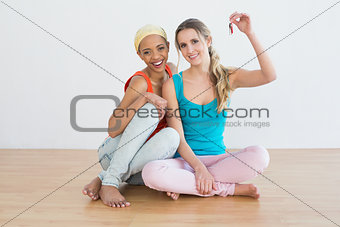 Cheerful female friends with house keys sitting on floor