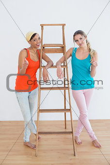 Female friends gesturing thumbs up against ladder in new house