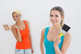 Portrait of two cheerful female friends holding paintbrushes