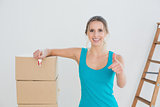 Woman with keys, boxes gesturing thumbs up in new house