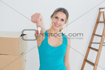 Woman holding out with key besides boxes in new house