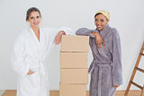 Female friends in bathrobes by boxes in new house
