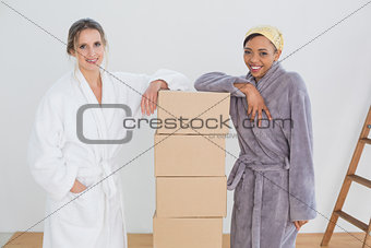 Female friends in bathrobes by boxes in new house