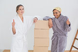 Friends in bathrobes with boxes gesturing thumbs up in new house