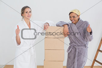 Friends in bathrobes with boxes gesturing thumbs up in new house