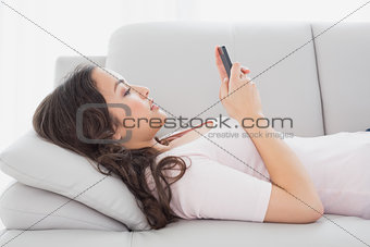 Relaxed young woman text messaging on sofa at home